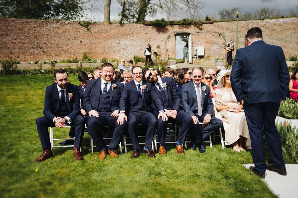 Wedding guests seated in rows on lawn watch ceremony proceedings.