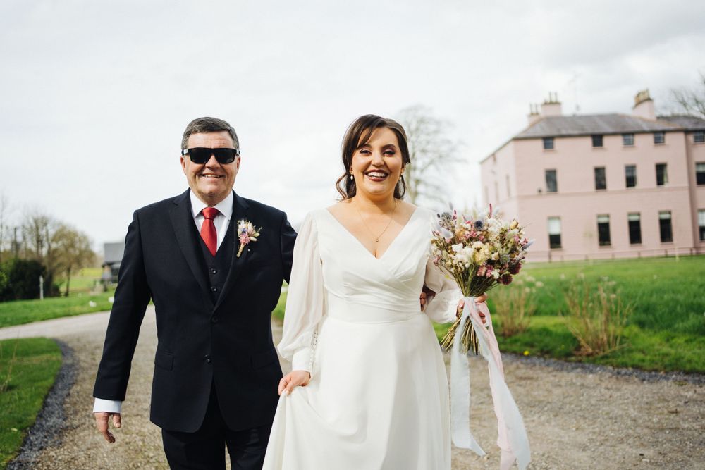 Wedding couple walking along path with pink mansion in background during springtime celebration.