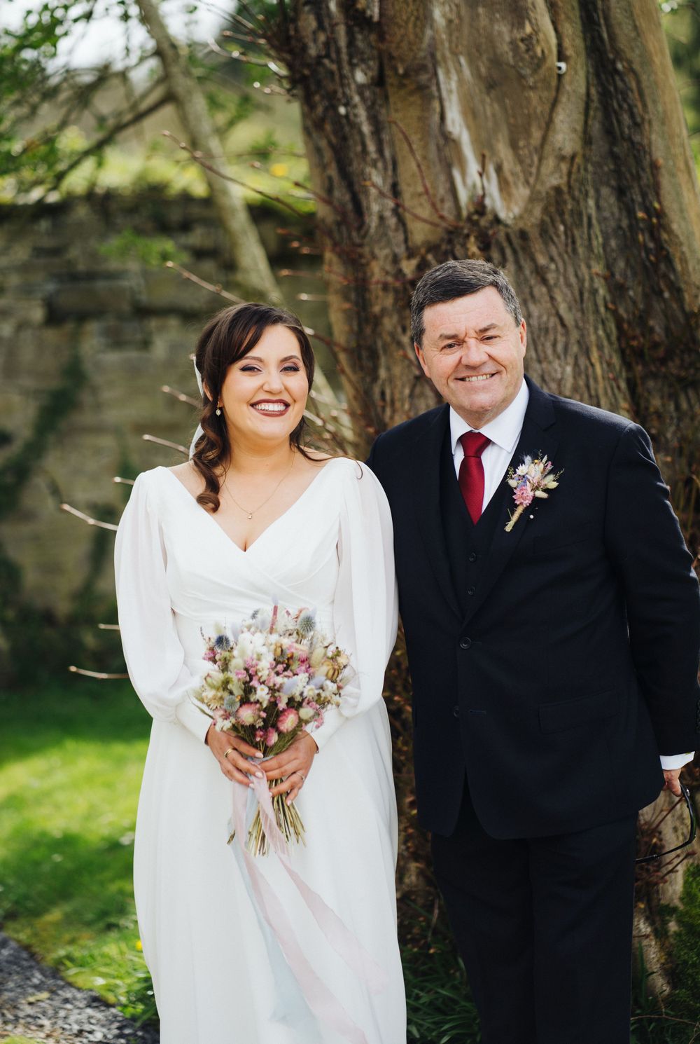 Happy couple poses under large tree during their spring wedding celebration.