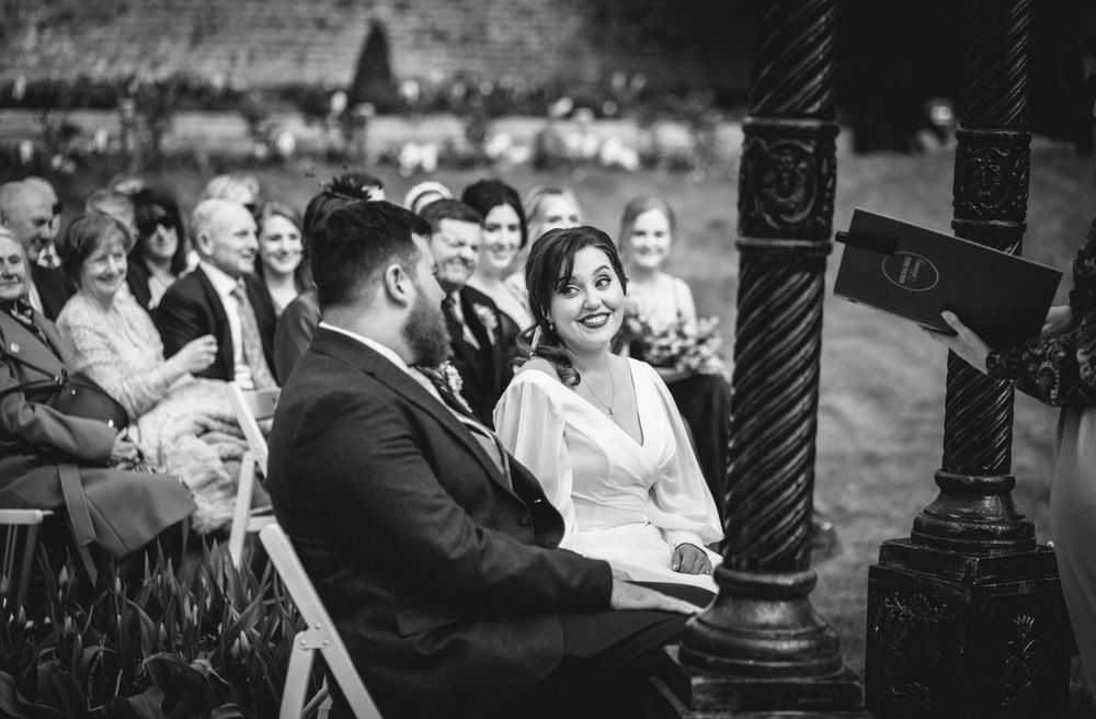 Black and white candid shot of wedding couple and guests during outdoor ceremony.