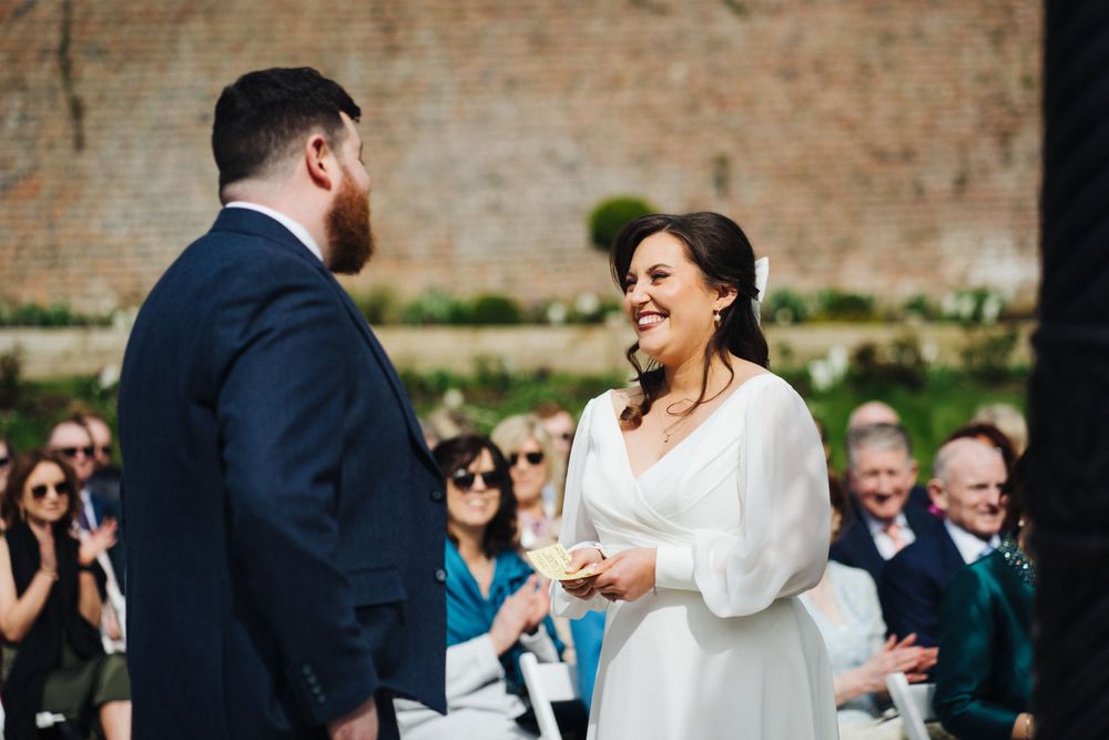 Joyful moment between couple during outdoor wedding ceremony against brick wall backdrop.