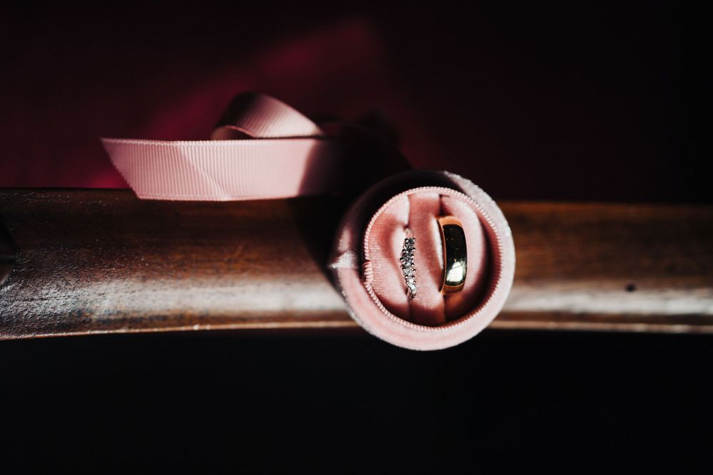 Pink ribbons and wedding rings displayed in artistic detail shot.