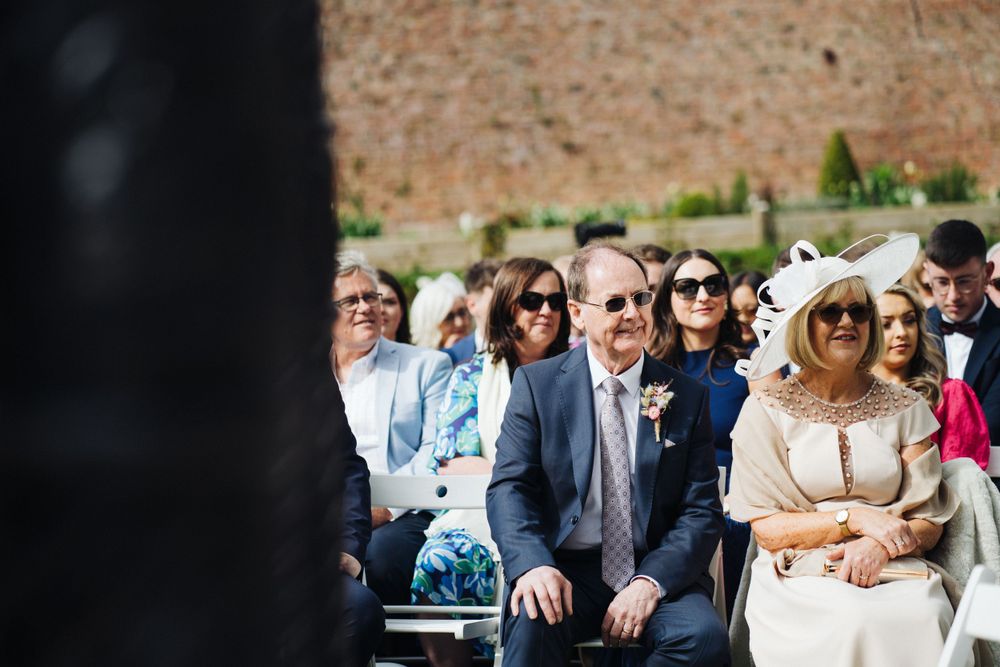 Wedding guests seated in rows of white chairs at an outdoor ceremony.