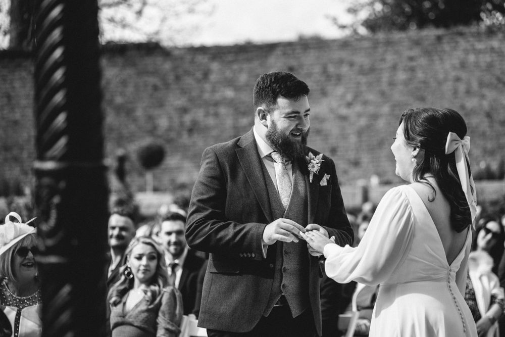 An outdoor wedding ceremony exchange of vows with guests seated in background.