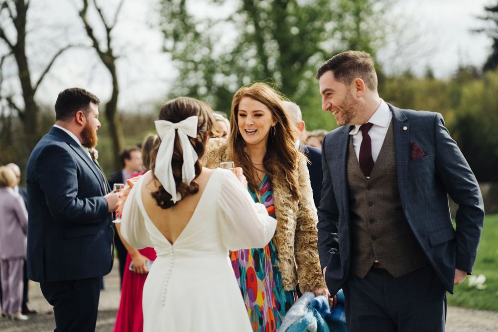 Wedding guests gather outdoors for a reception celebration with formal attire and natural scenery.