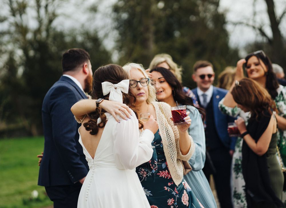 Wedding guests share hugs and laughter during an outdoor celebration.