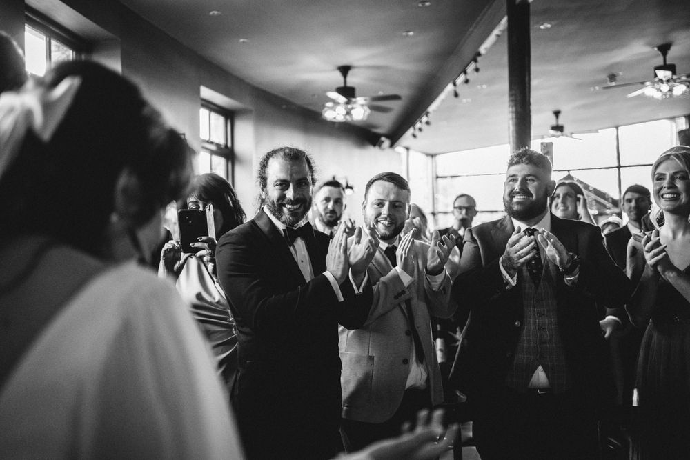 Black and white photo of wedding guests reacting with joy during indoor reception.