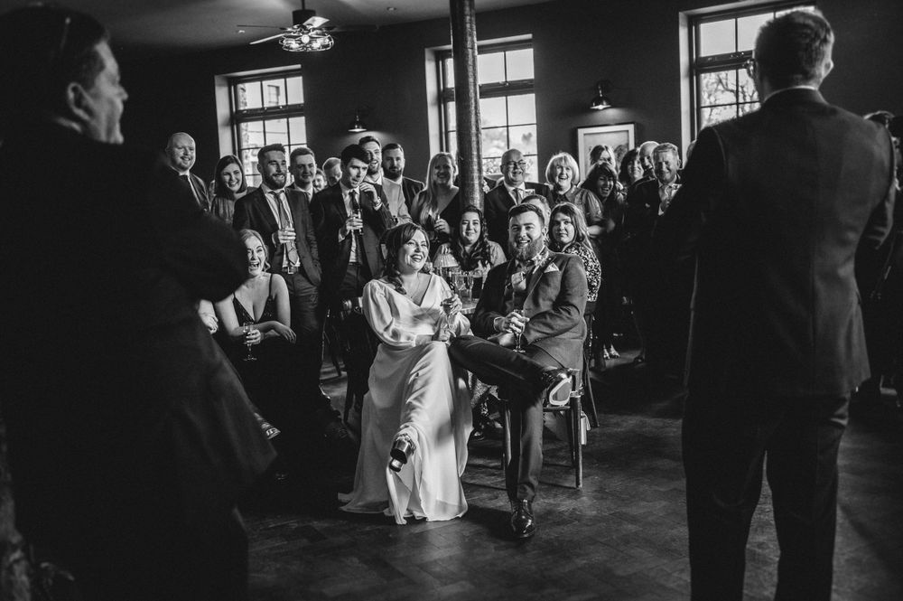Wedding guests seated in rows watch intently during an indoor ceremony in a rustic venue.