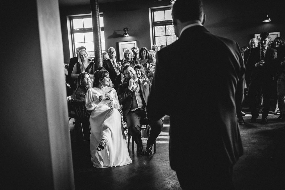 Wedding guests gather in a room with exposed brick walls during a reception.