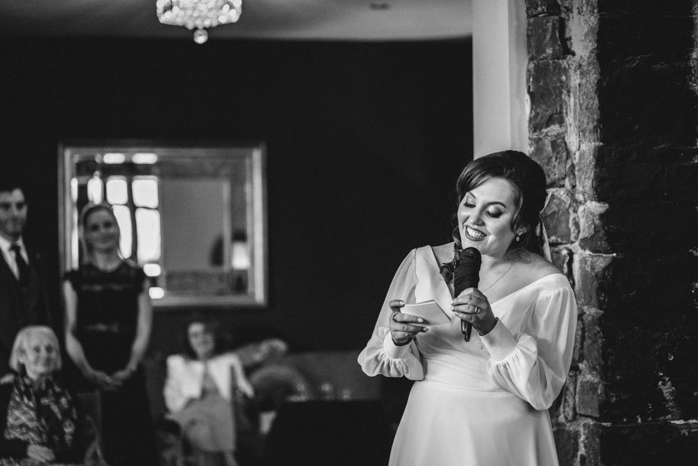 A speaker in white delivers emotional remarks during an indoor wedding reception.