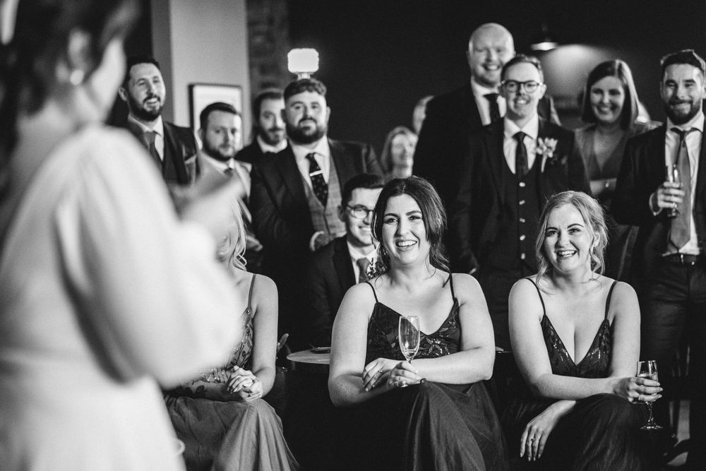 Wedding guests react with smiles and laughter while watching a moment during the celebration.