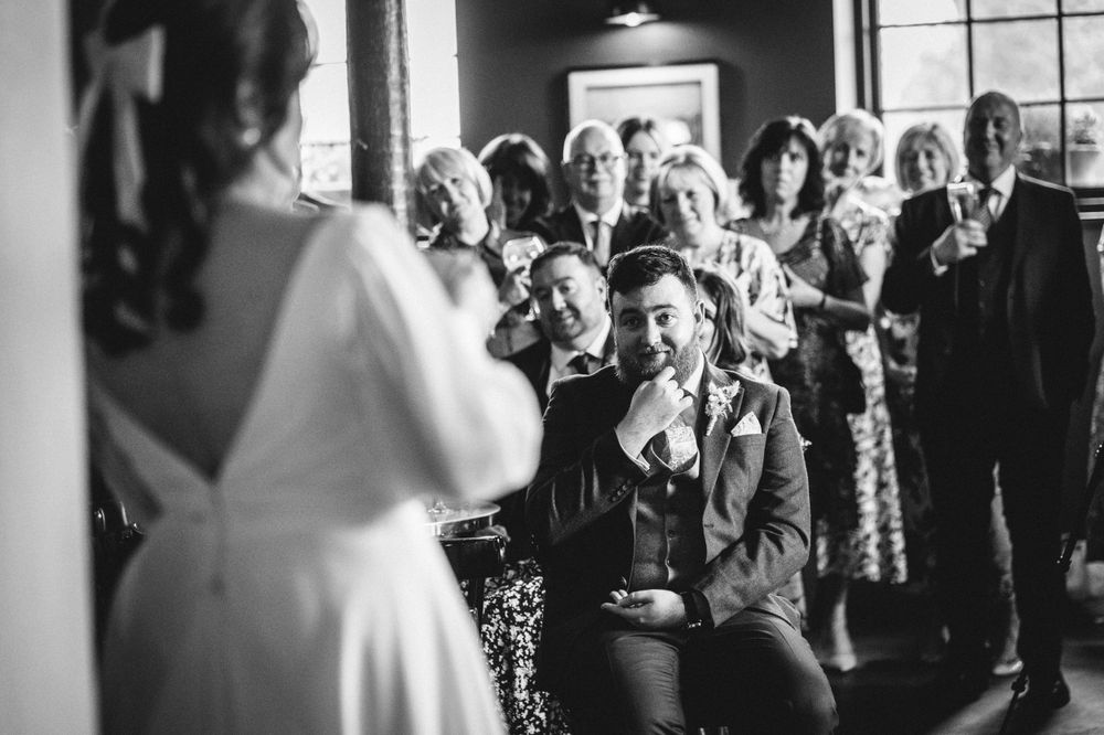 Wedding guests gather to watch speeches during an indoor reception.