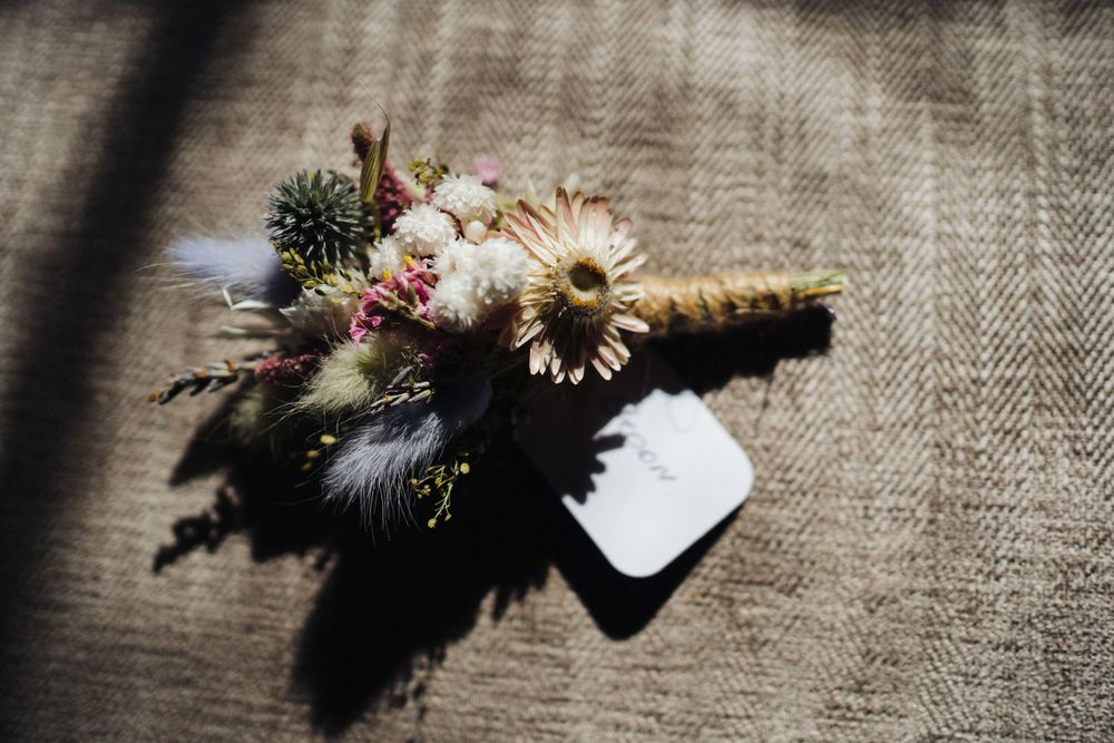 Delicate wedding boutonniere with daisies and small flowers tied with twine on textured fabric.