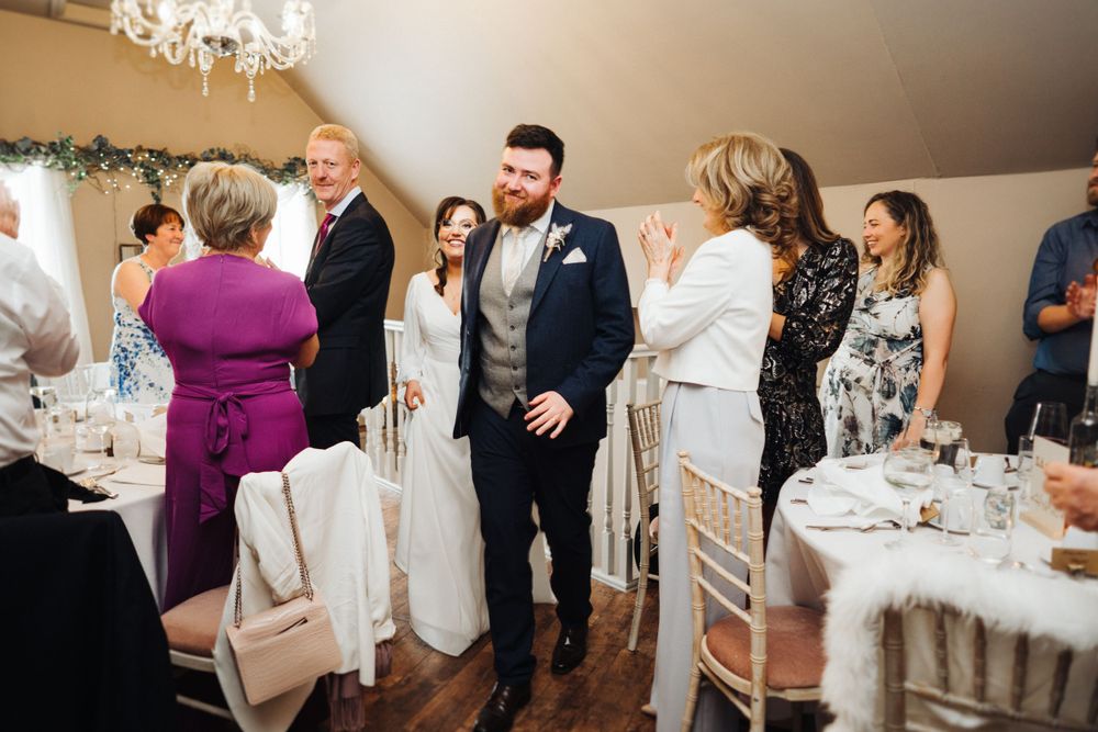 Wedding celebration in an elegant reception room with chandelier and decorated tables.