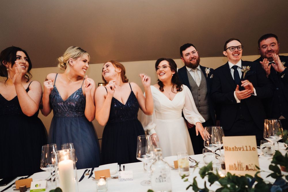 Wedding party shares candid moment of laughter at decorated reception table.