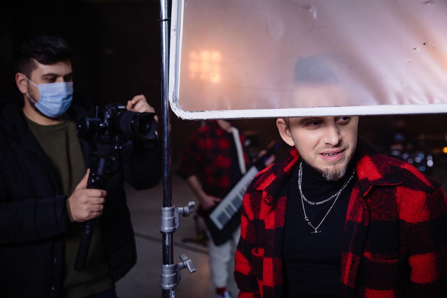 Performance or recording session in dimly lit studio with red plaid shirt visible.
