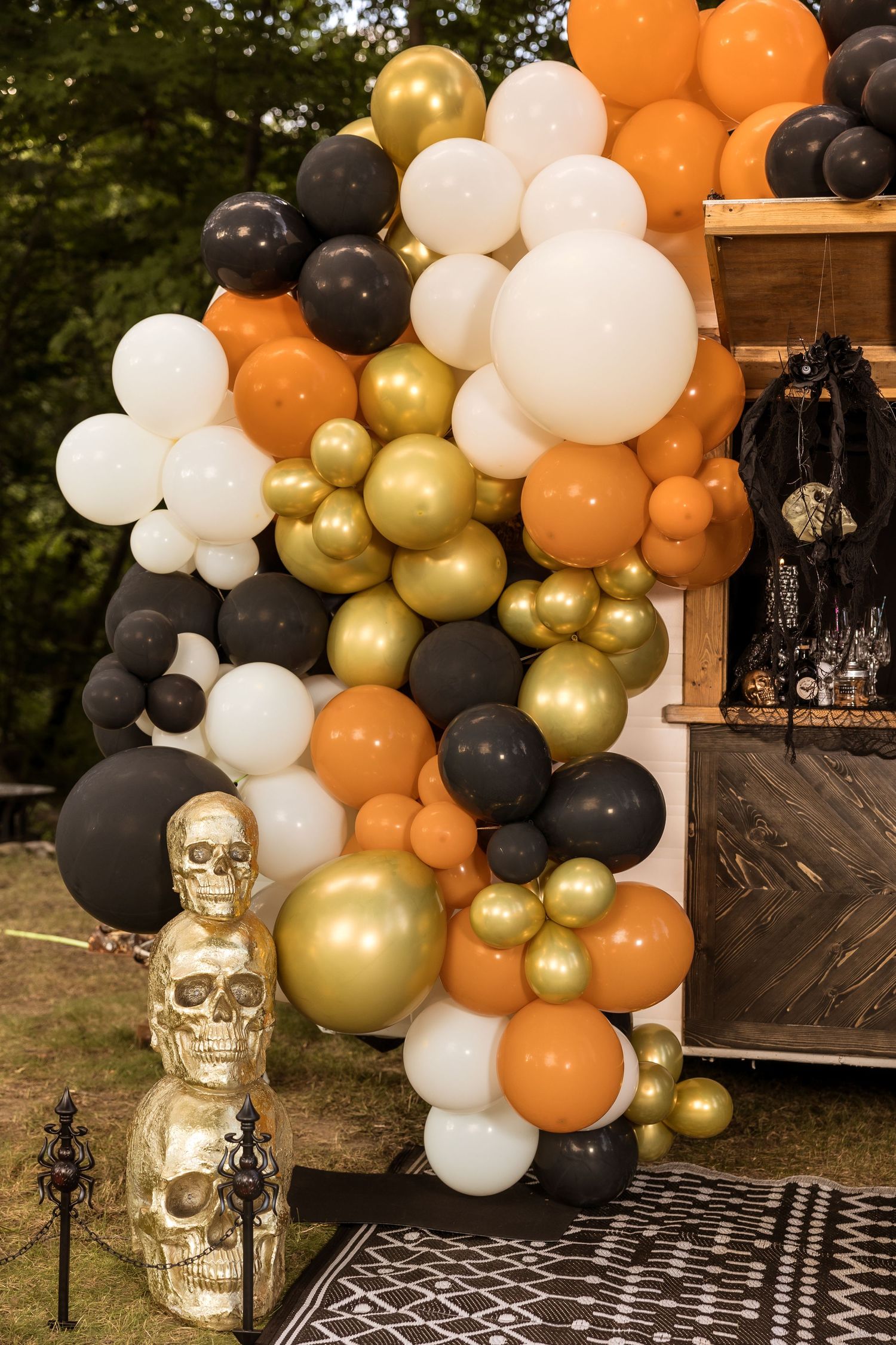 Elaborate balloon arch in orange, gold, black and white with decorative skull props.