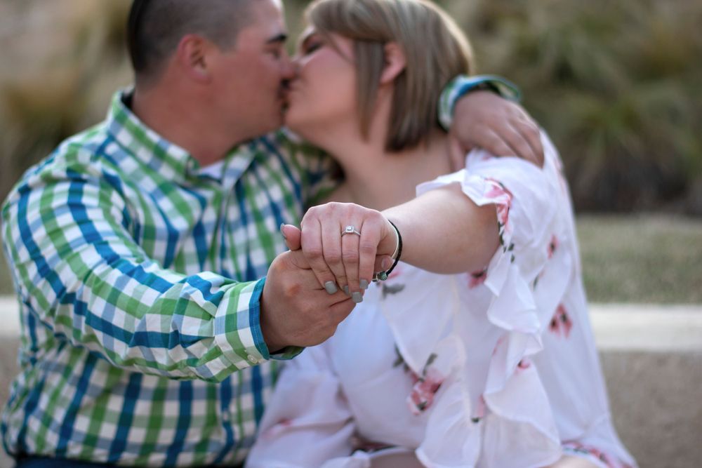 A newly engaged couple kisses while they show off the engagement ring