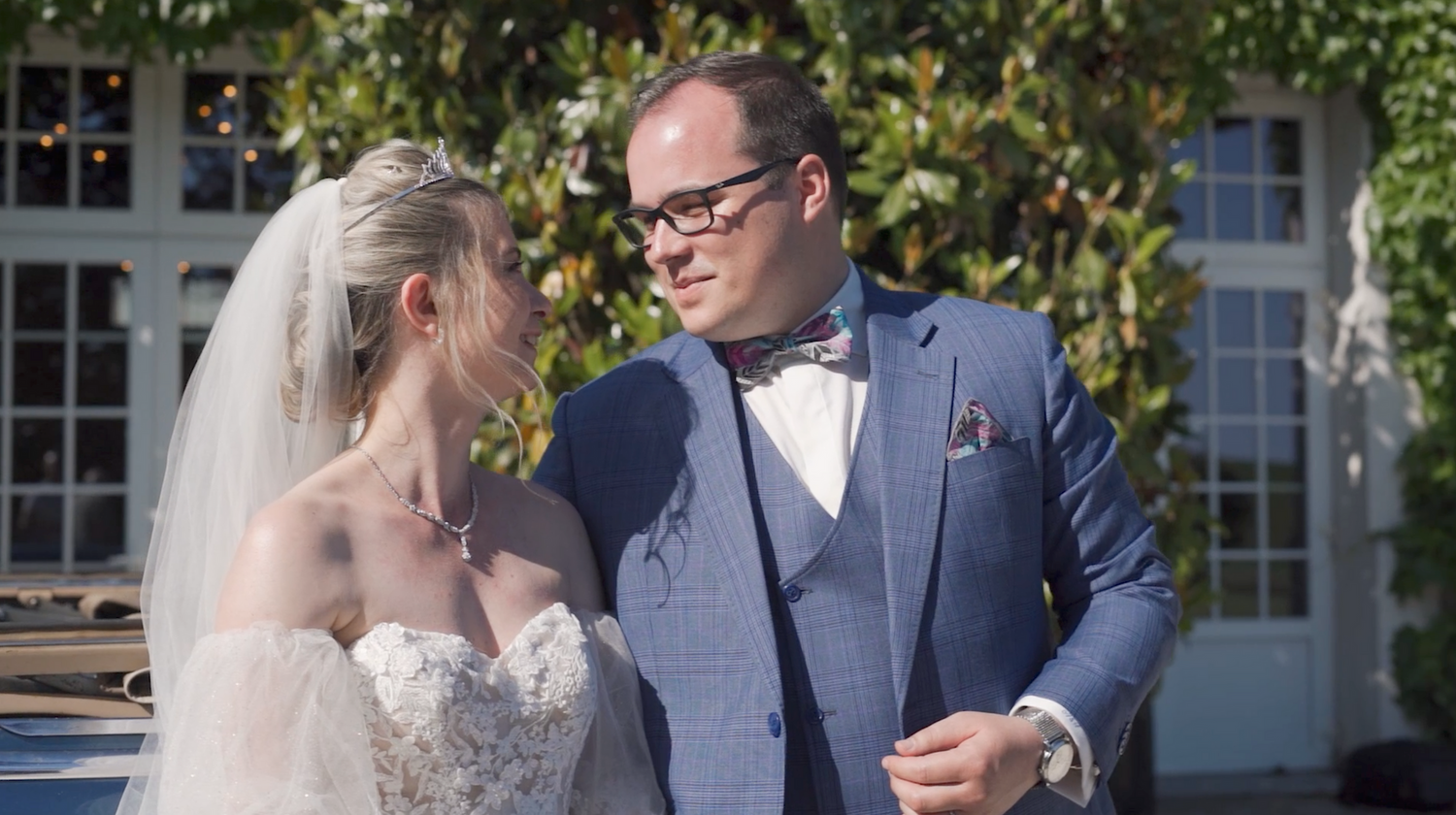 A romantic wedding couple poses together in a manicured garden setting with elegant hedges and greenery.