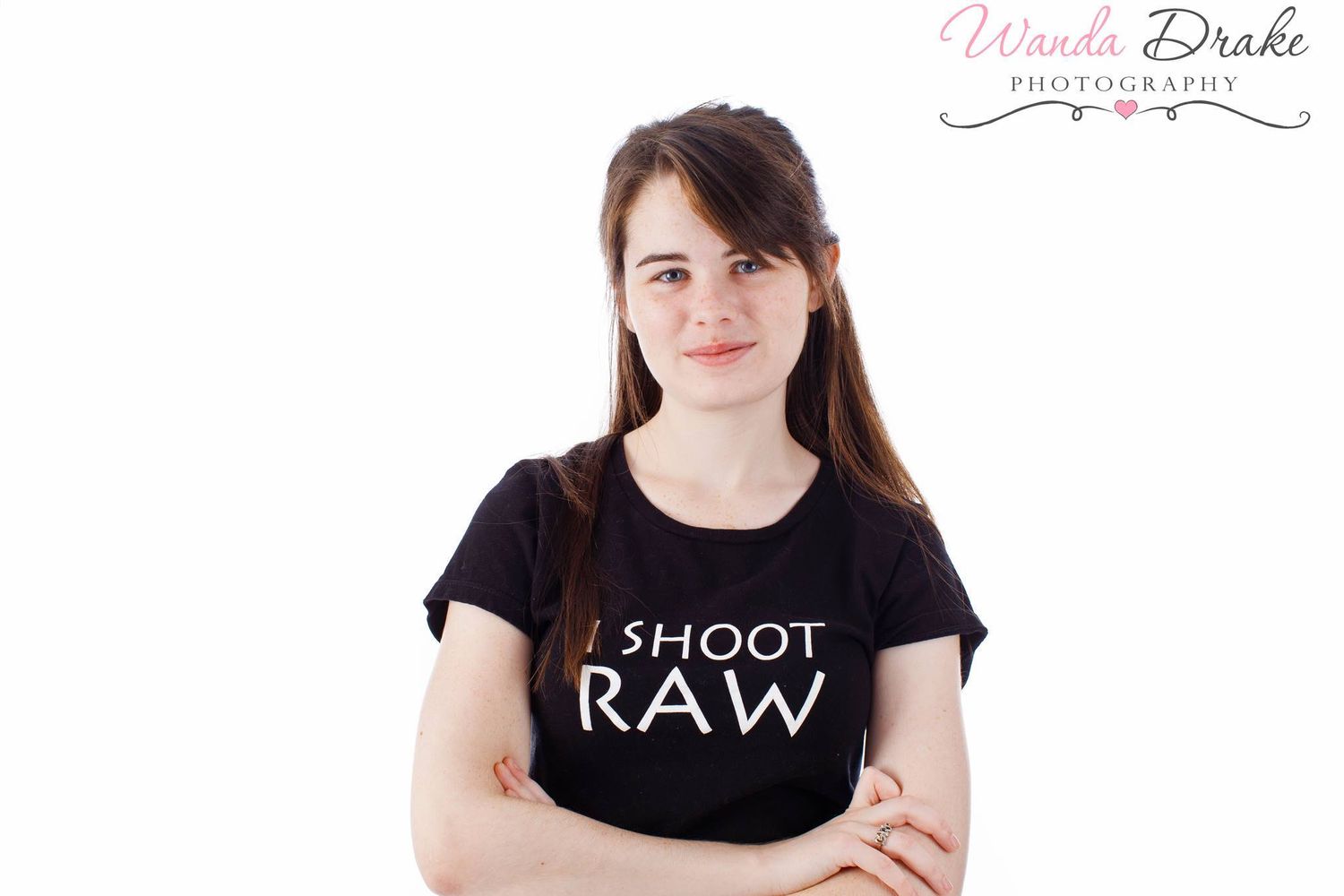 A photographer wearing a black 'I SHOOT RAW' t-shirt stands with arms crossed.