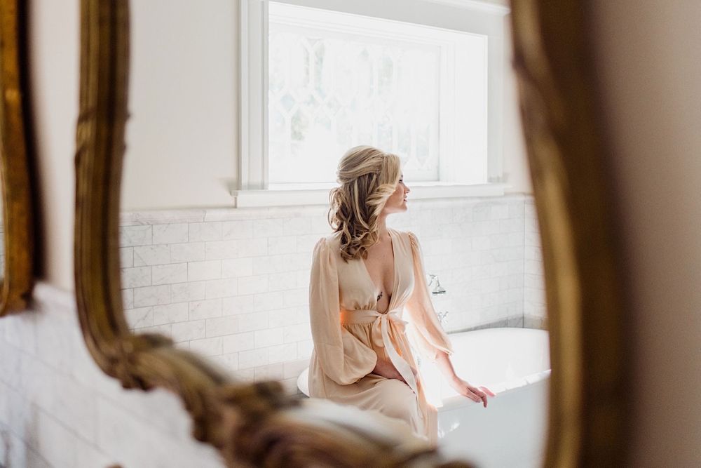 Bride in a silk robe sitting on a clawfoot bathtub in the mirror