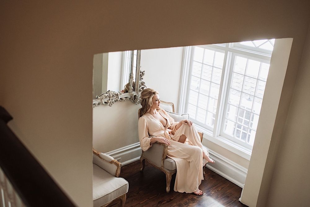 Bride sitting on a love seat in peach silk robe and looking out the window