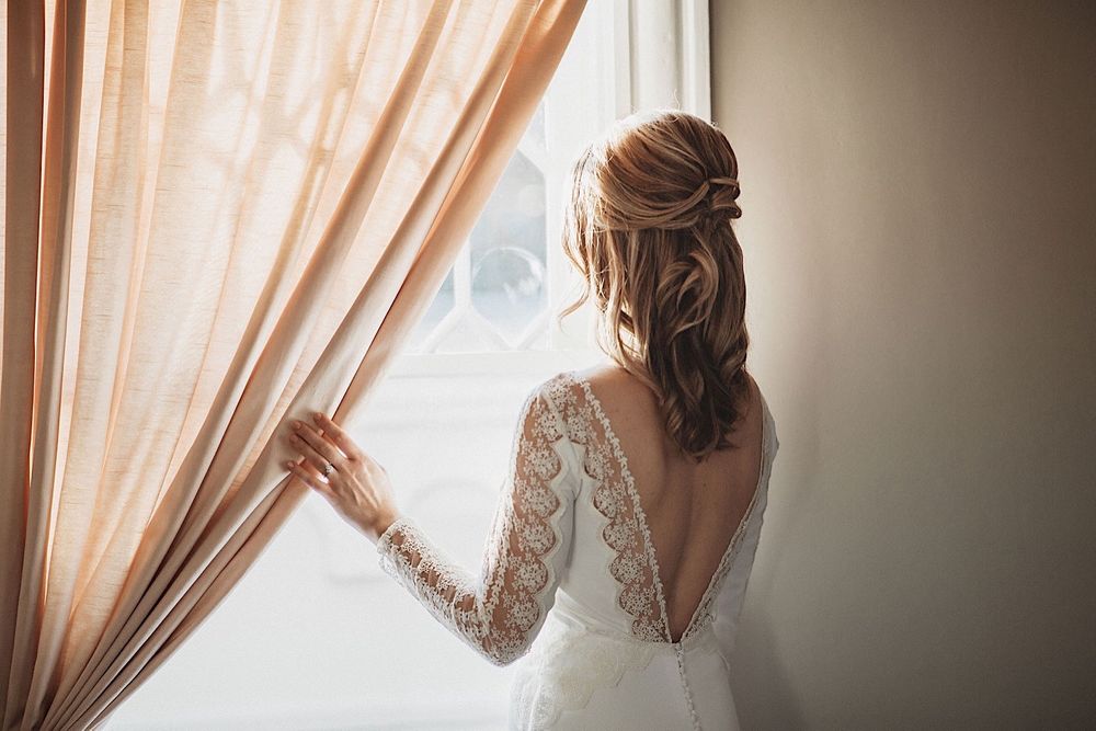 bride looking out the window holding onto a pink curtain
