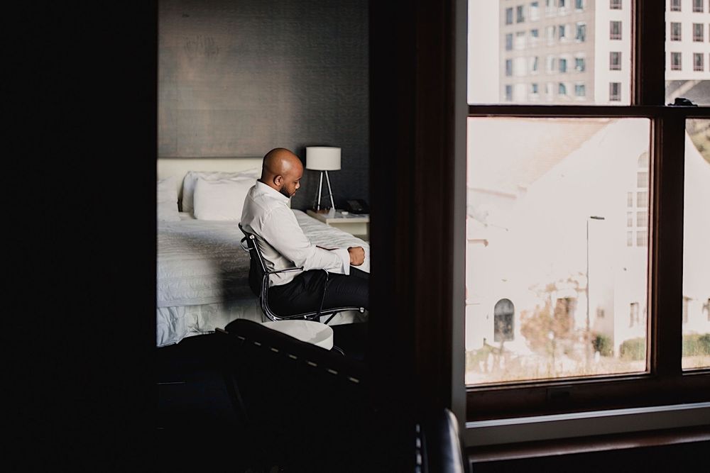 groom sitting on hotel bed putting on shoes