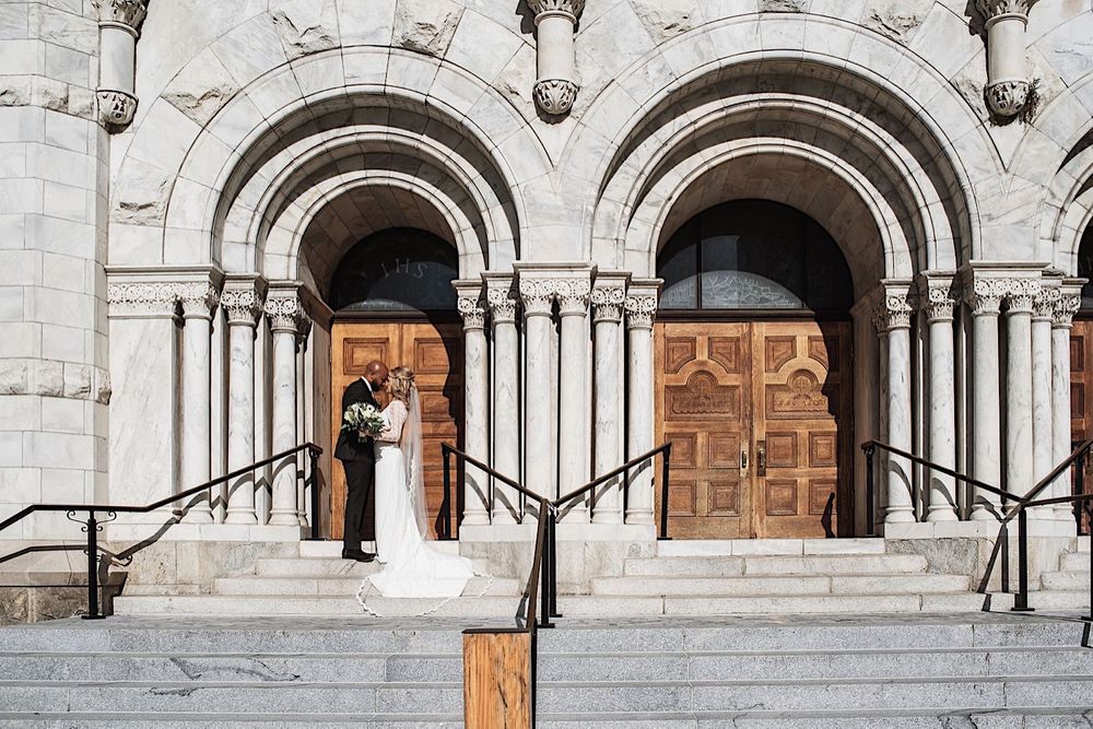 bride and groom standing in front of arched doorway on the steps of sacred heart church in downtown tampa
