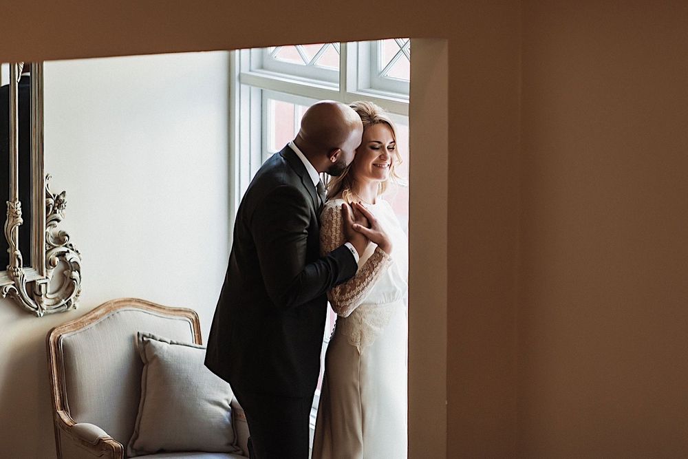 groom hugging bride from the back near the window at the orlo