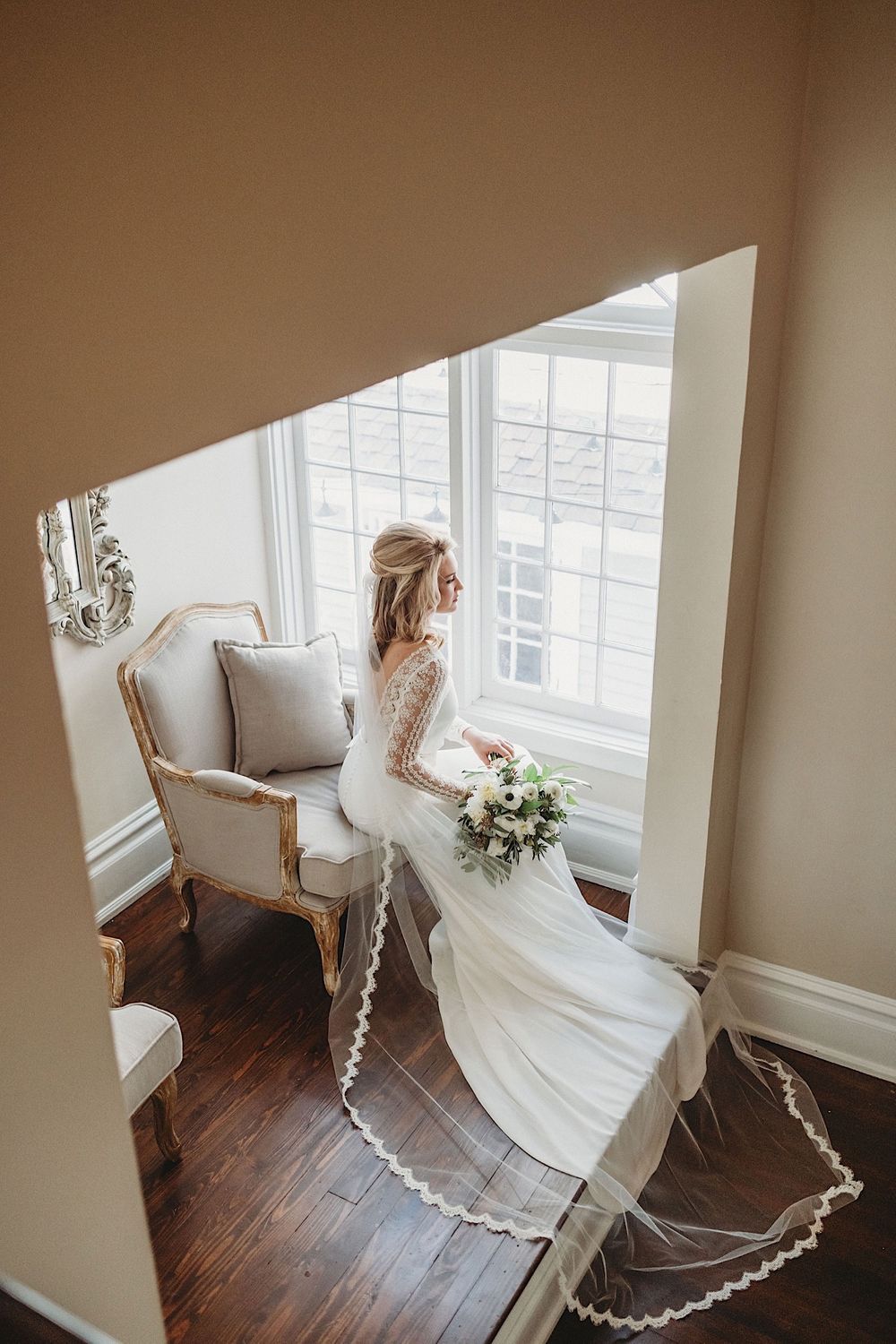 bride sitting in chair holding bouquet and looking out the window