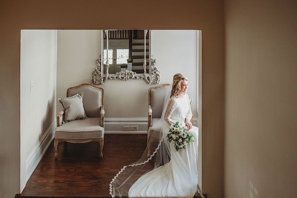 bride sitting in chair holding bouquet and looking out the window