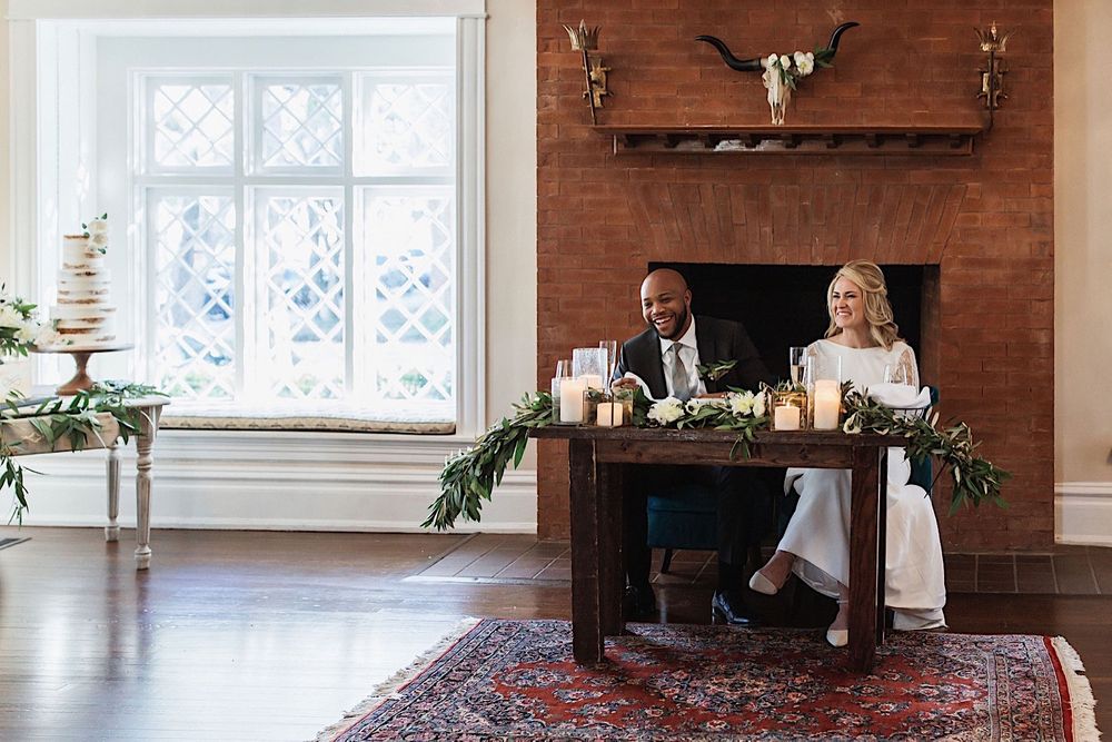 bride and groom sitting at the sweetheart table and laughing at their wedding