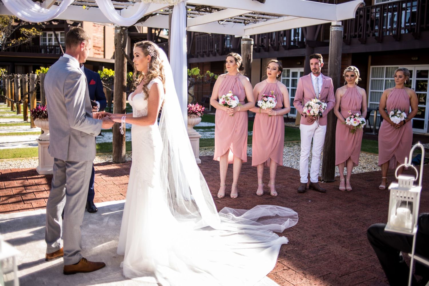 Wedding ceremony under covered pavilion with pink-dressed attendants and flowing white decor.