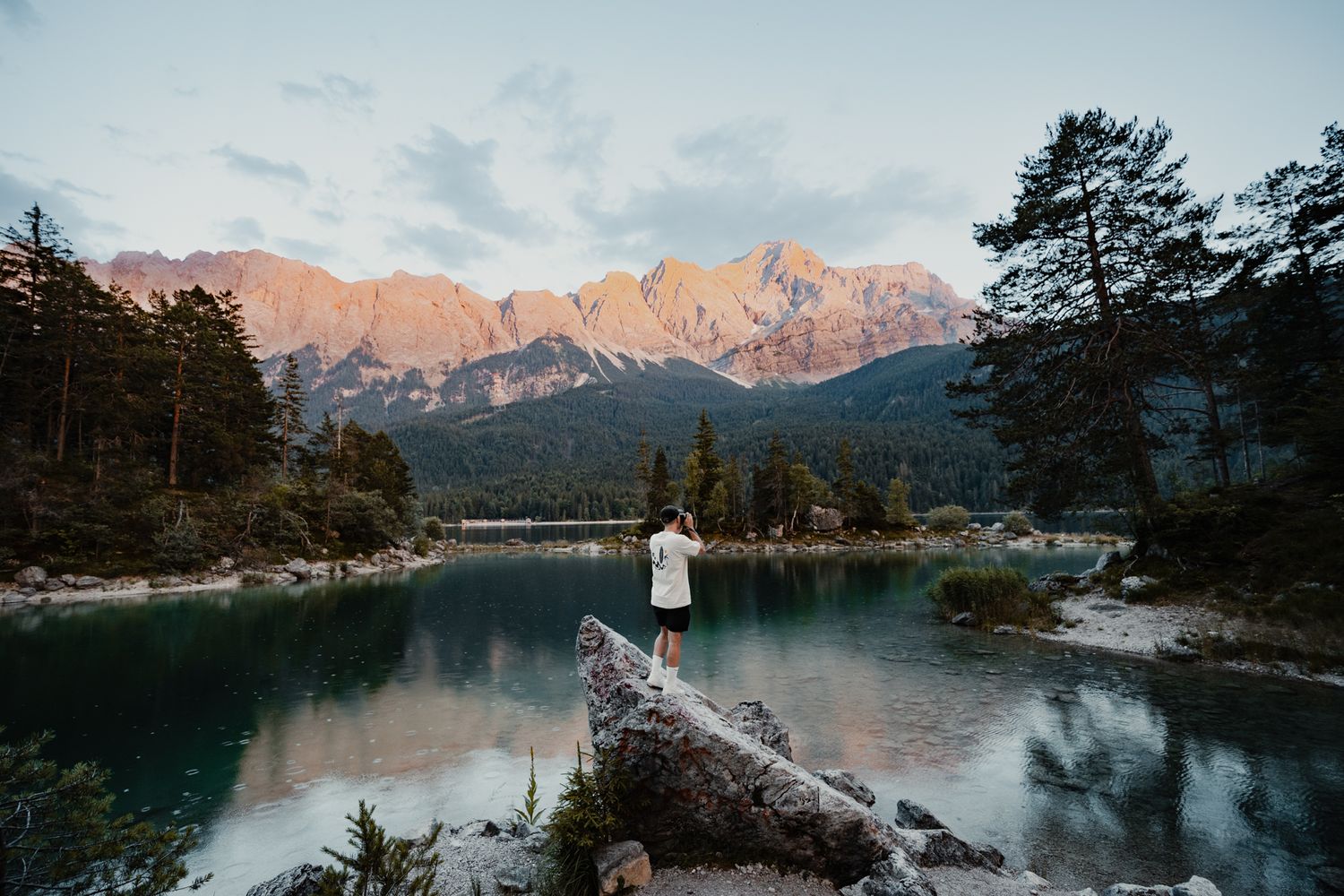 Scenic mountain lake view with pine trees and snow-capped peaks during sunset in the Alps.