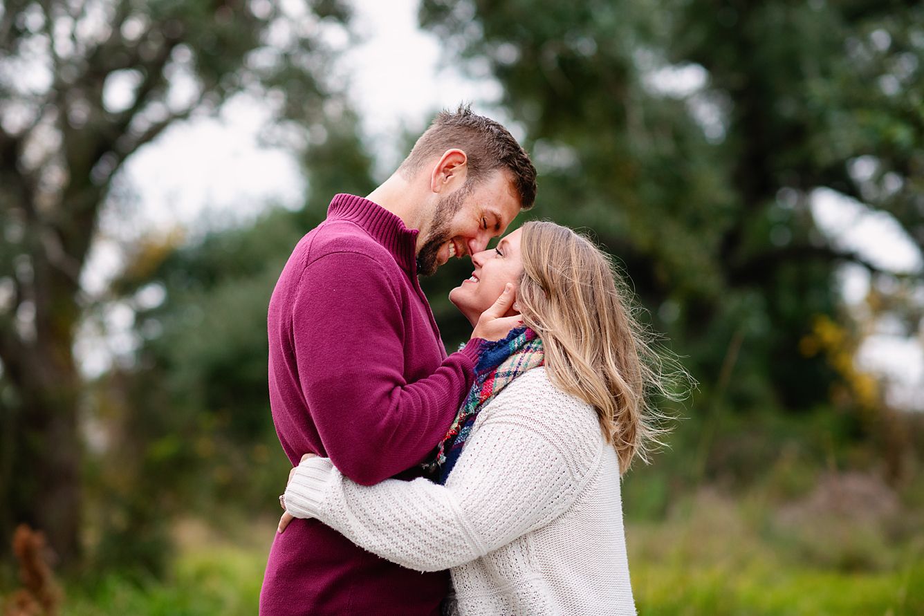 Romantic couple in sweaters smiling face to face in an outdoor autumn green landscape.