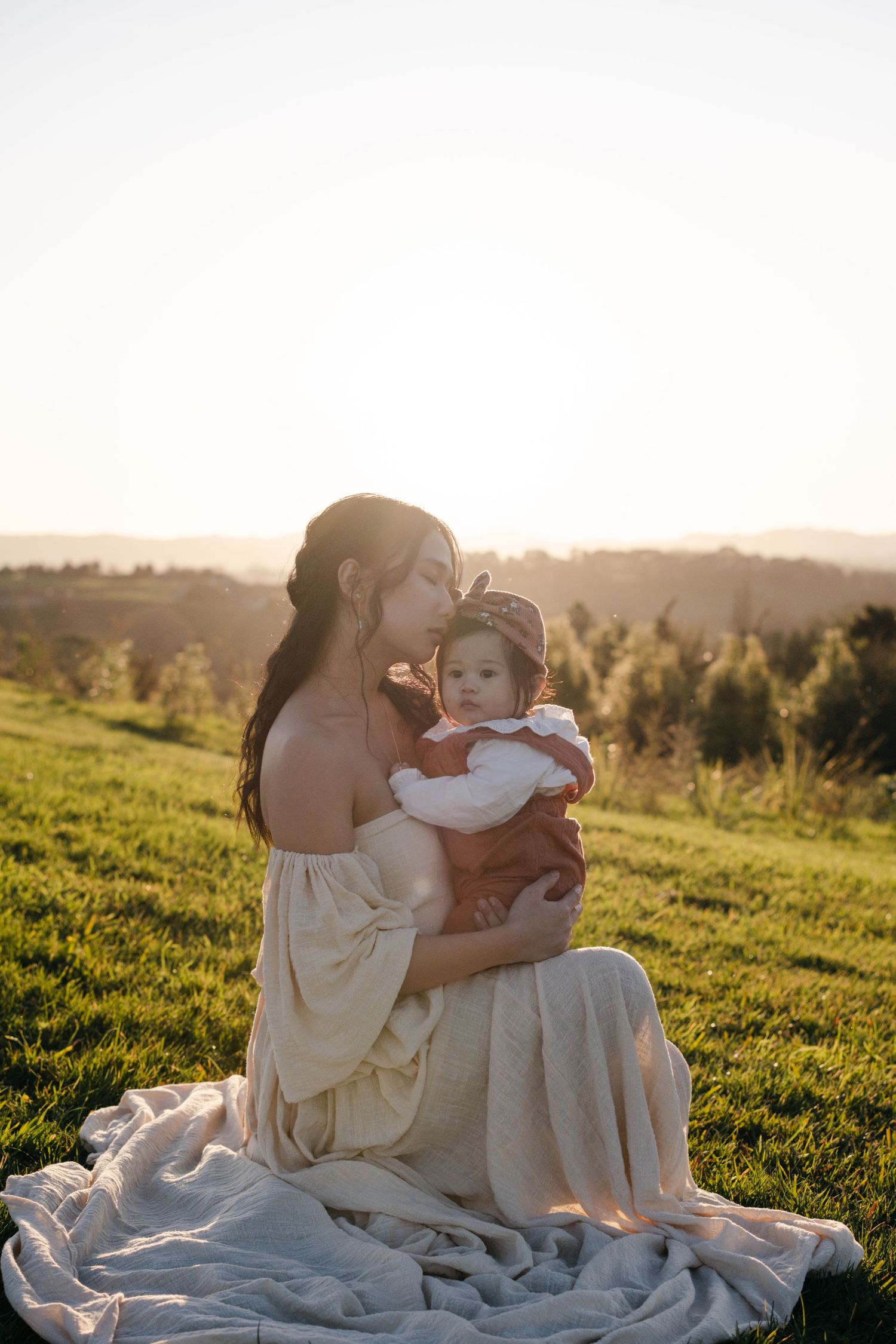Family bonding moment on white blanket in sunlit meadow during golden hour.