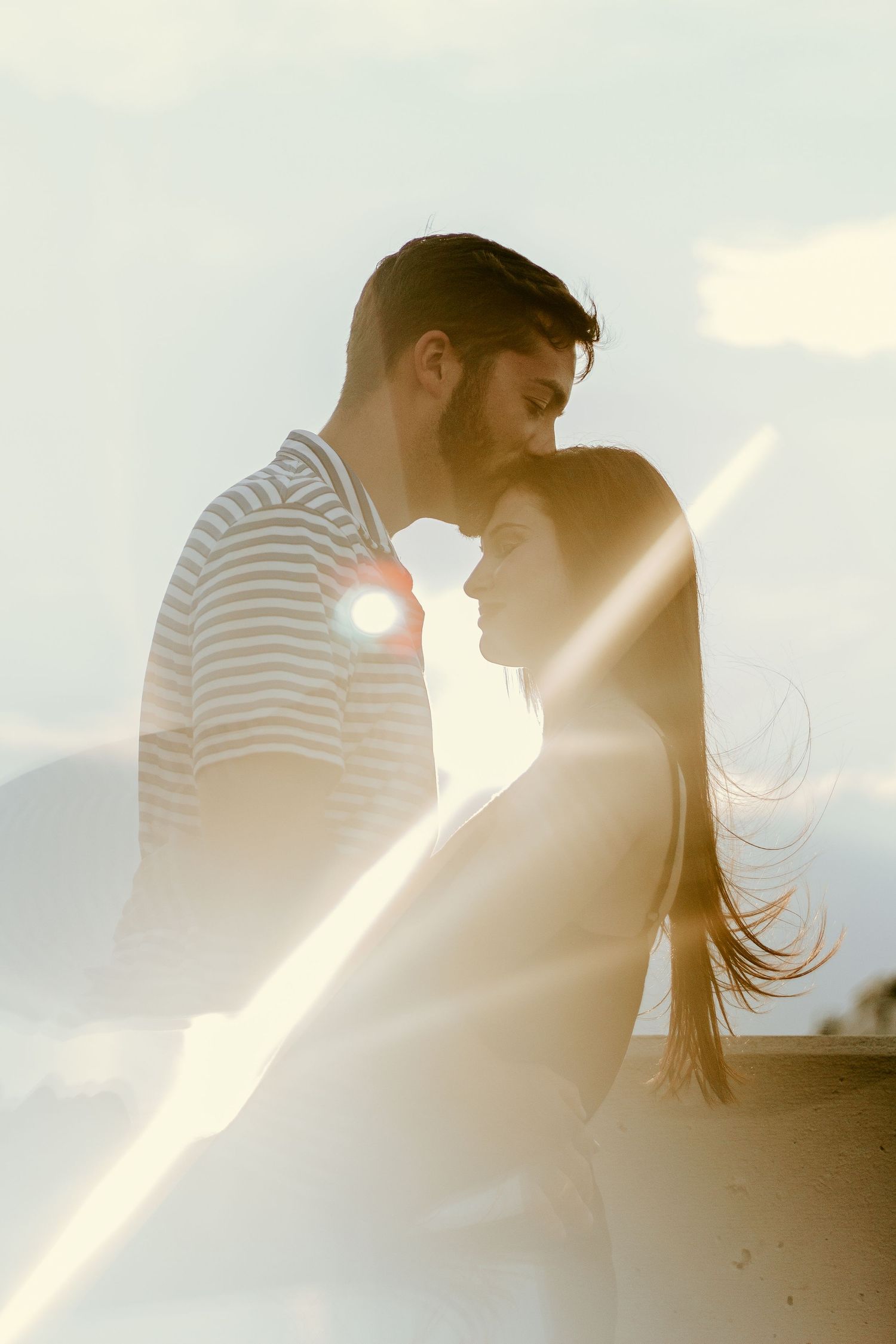 Backlit couple in intimate moment with sunlight creating ethereal glow.