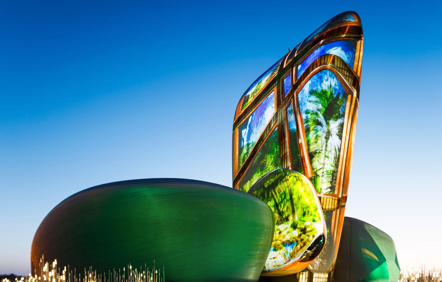 Green glass sculptural installation with curved reflective surfaces at sunset.