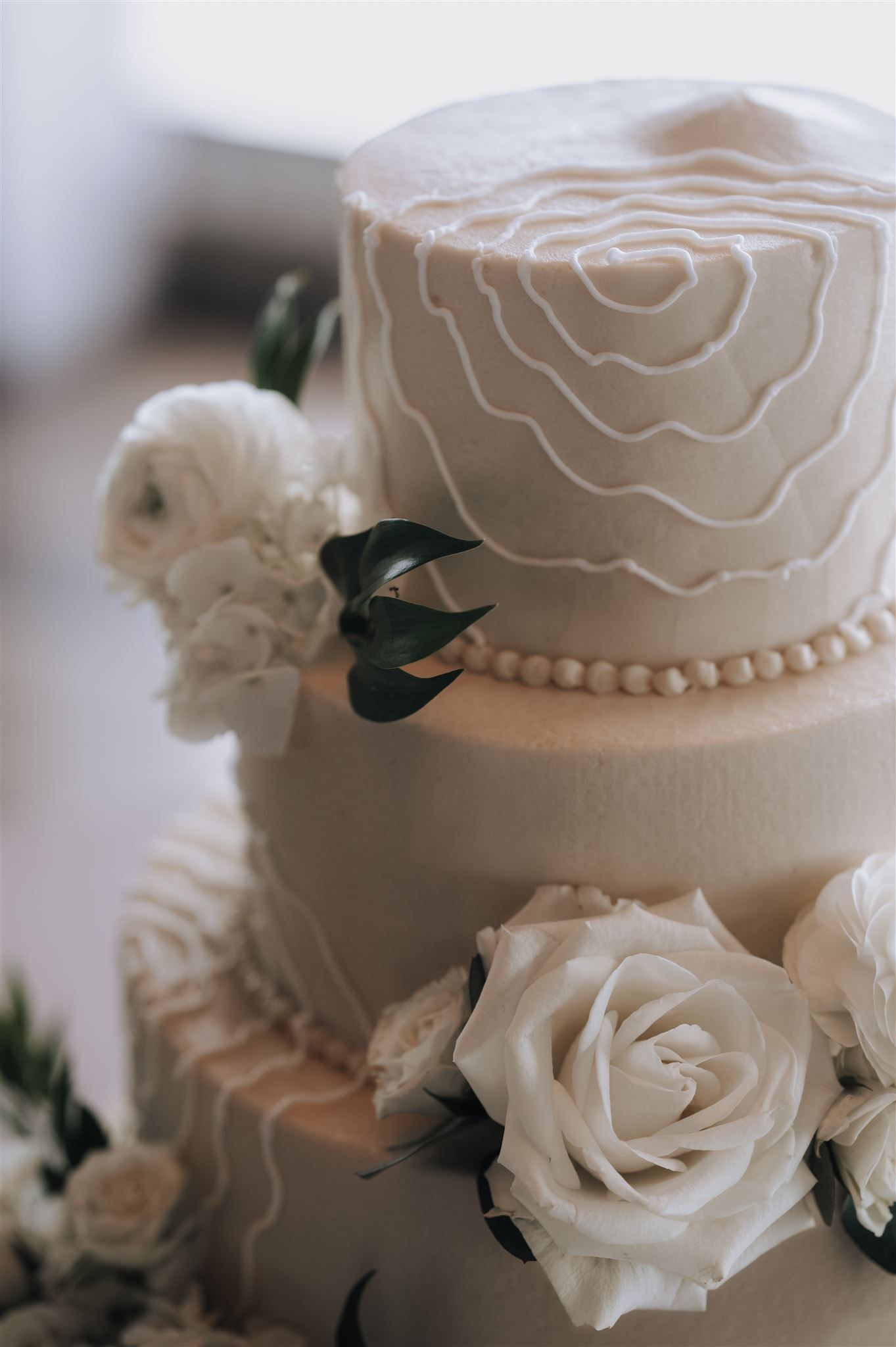 Close-up of white wedding cake tiers with delicate rose design and fresh flower decorations.