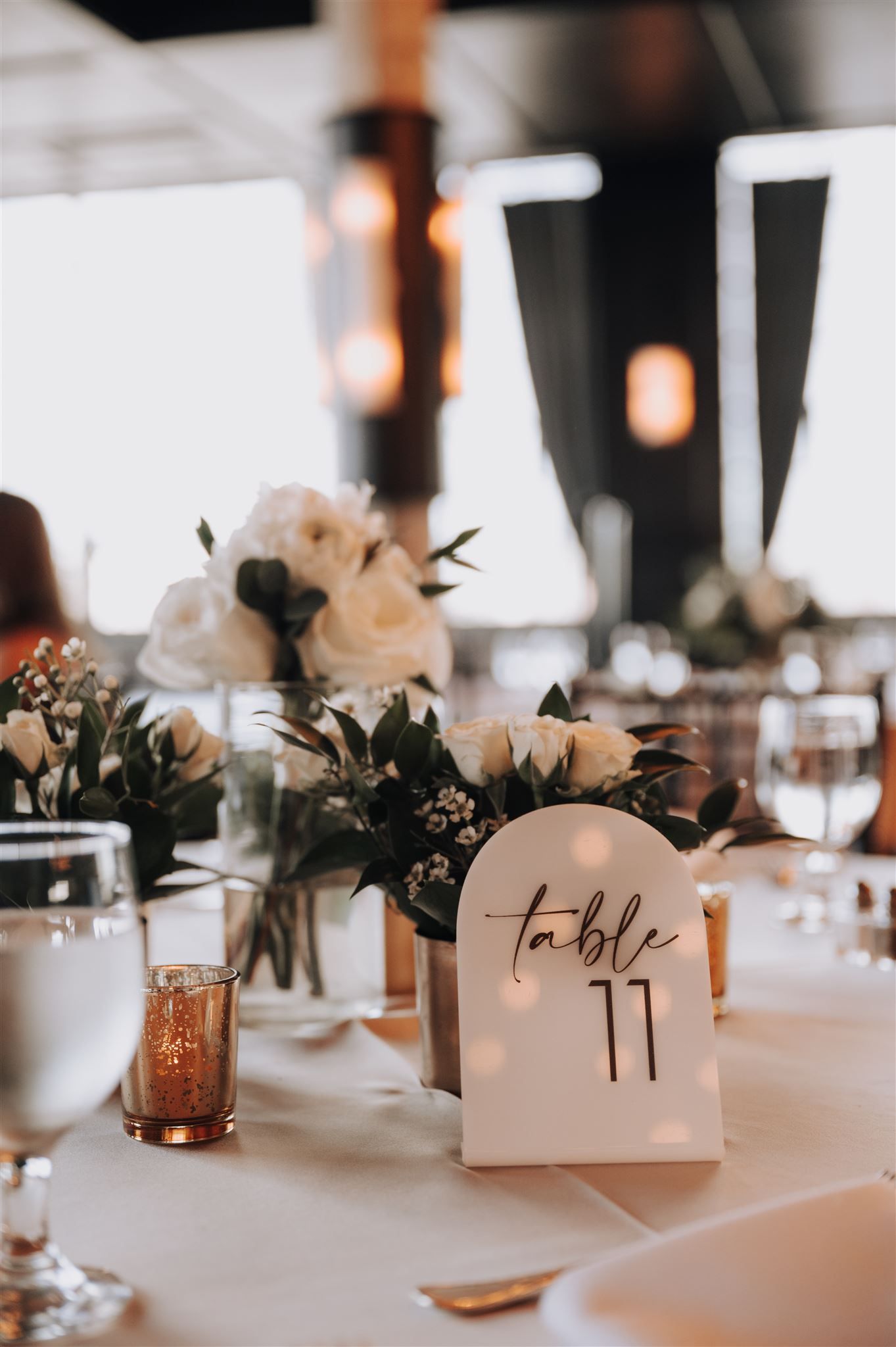 Wedding reception table setting with floral centerpiece and table number 11 in modern calligraphy.