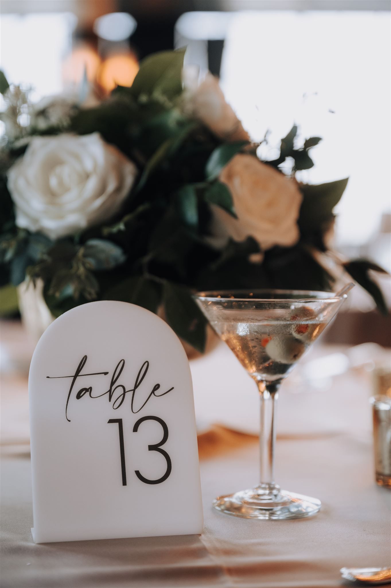 Wedding reception table detail with table number 13 and martini glass next to white roses.