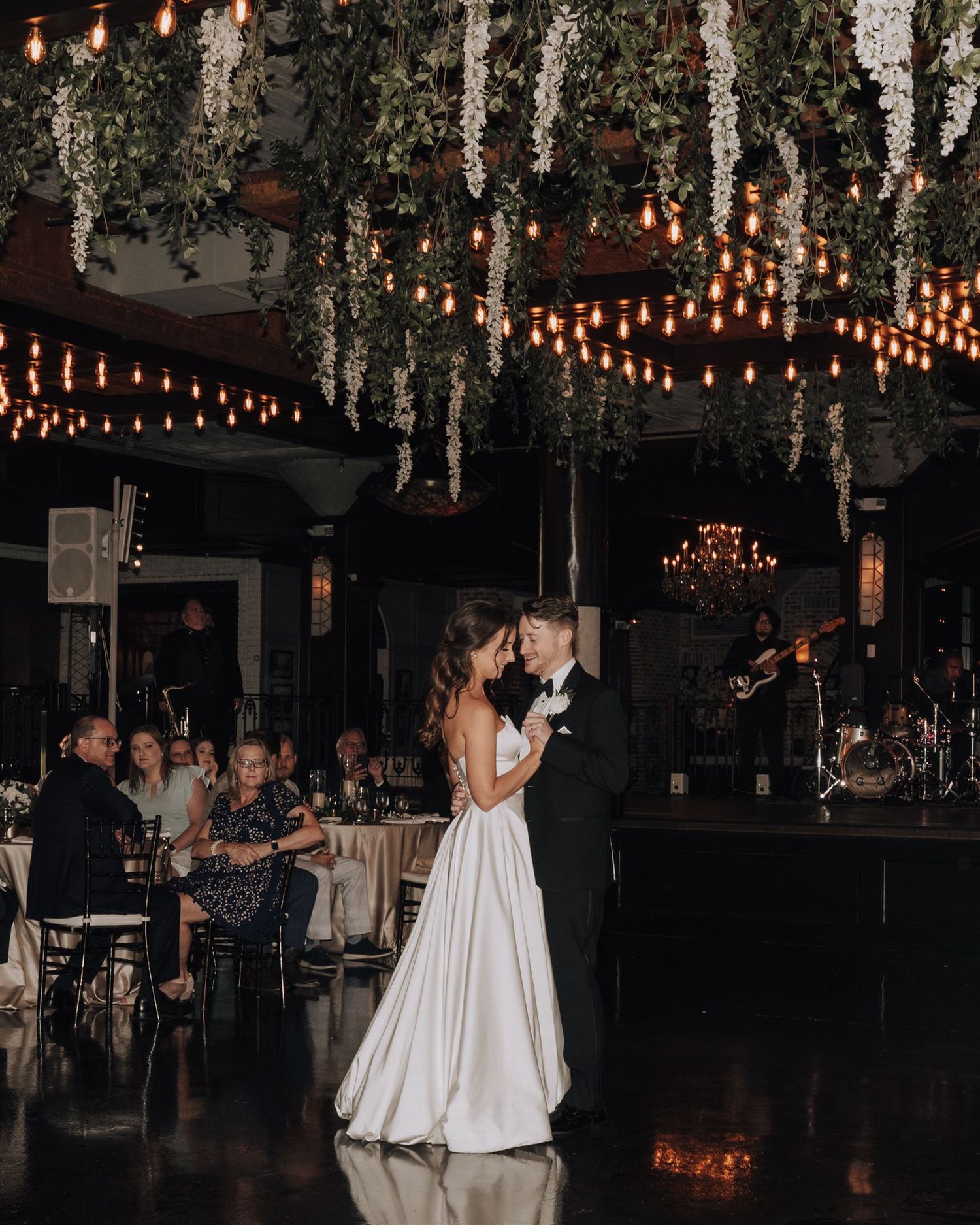 Newlyweds dance beneath cascading greenery and string lights at their reception.