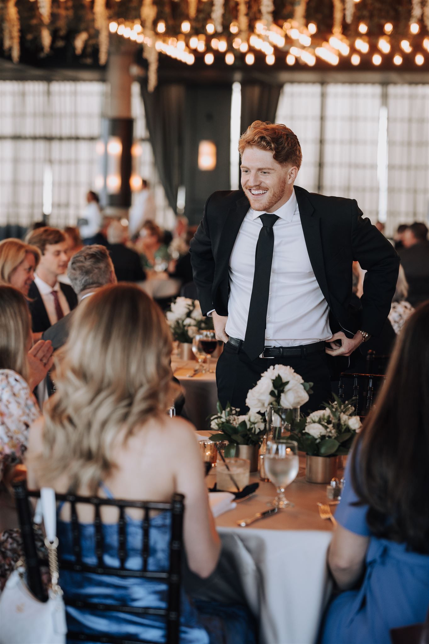 Guest entertains dinner table at wedding reception under decorative lighting.