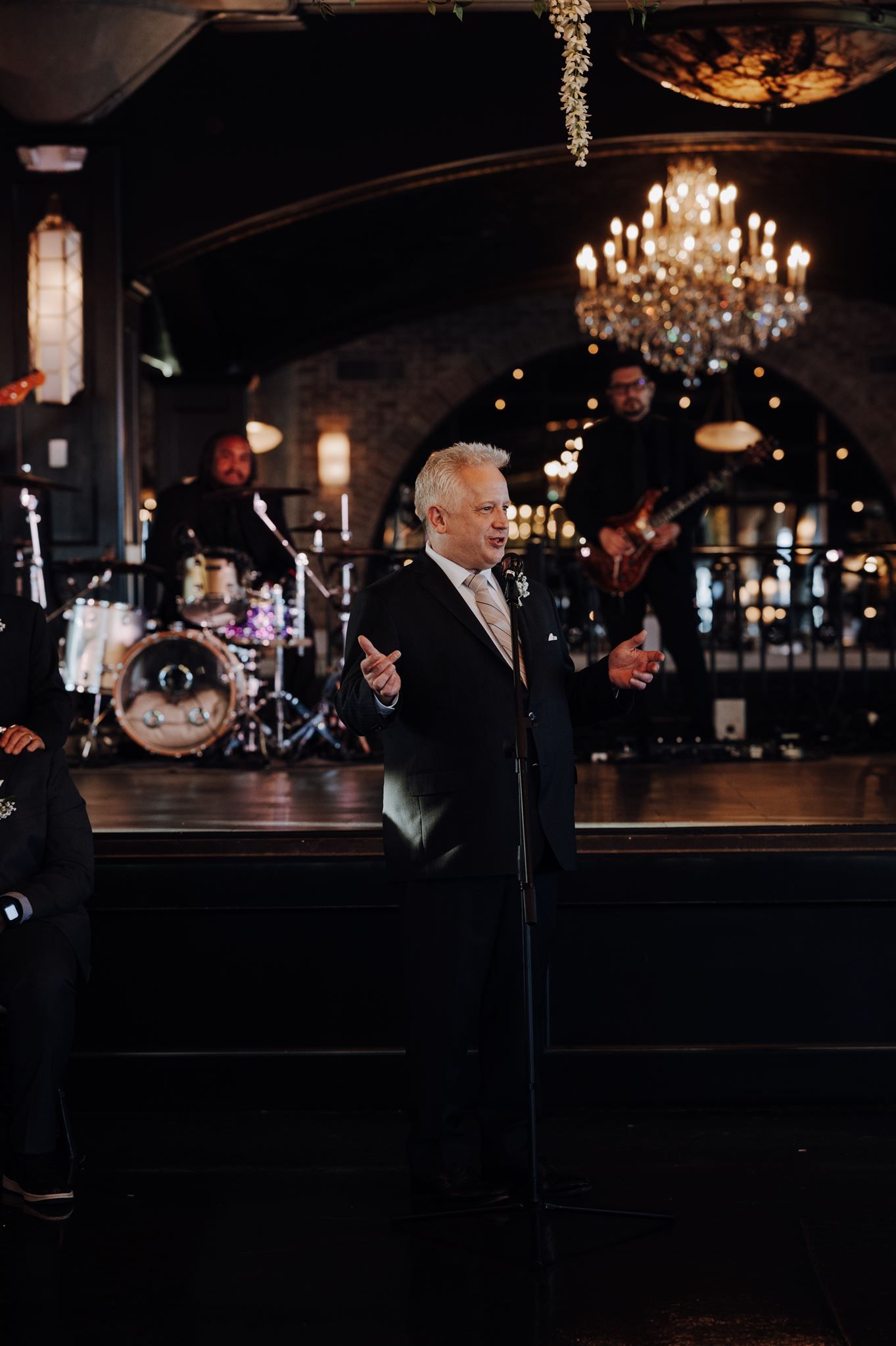 Performer sings at elegant wedding reception venue with chandelier and stage.