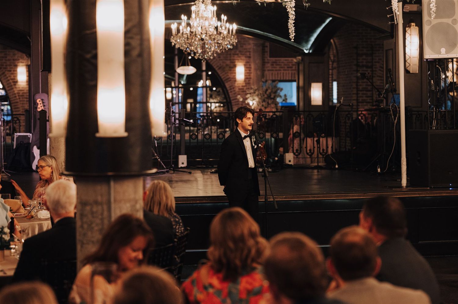 Dimly lit reception venue with chandelier and guests seated at tables during evening event.