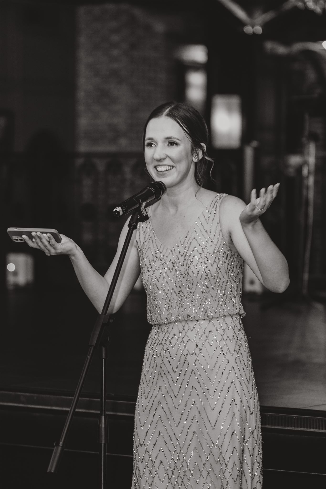 Guest in sparkly formal dress gives an animated speech at wedding reception.
