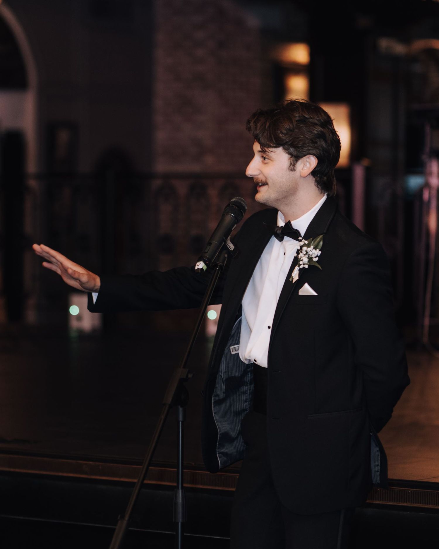 Wedding guest in black tuxedo delivers a speech at the reception microphone.