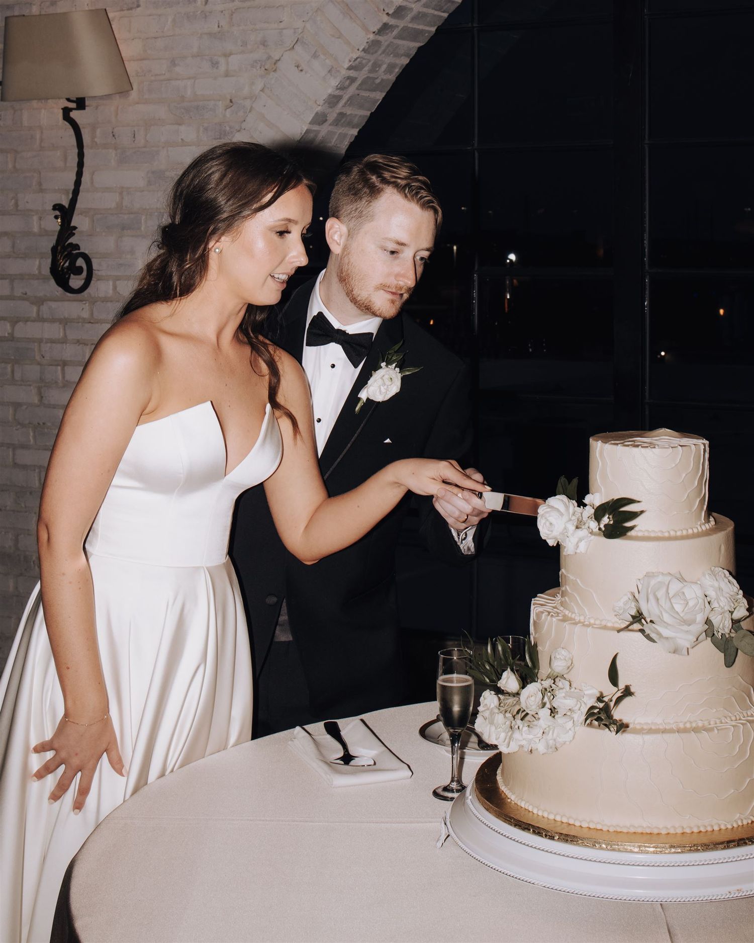 Couple cuts their elegant white wedding cake decorated with floral details at their reception.