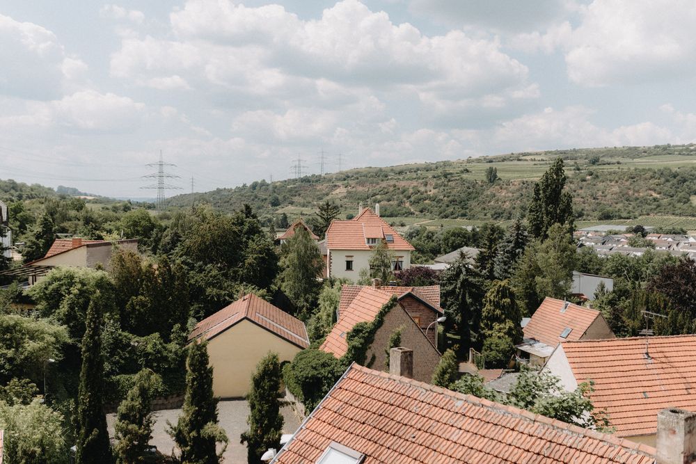 Aerial view of red-roofed houses and buildings nestled in a hillside neighborhood with power lines visible.